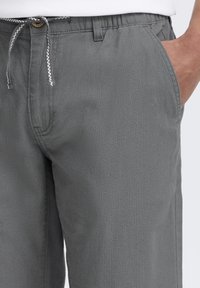 Pantalons à taille élastique grise avec cordon de serrage, quatre poches, coupe droite et tissu texturé. Présente des surpiqûres de contraste sur les bords.