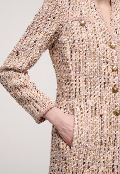 Pink tweed jacket with gold and multicolor threads. Features a v-neck, front pockets, and gold buttons with embossed logo accents.