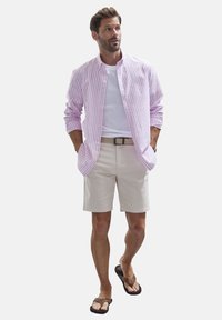 Männliches Outfit mit einem pink-weiß gestreiften Hemd mit Knöpfen, einem weißen T-Shirt, beigen Shorts und braunen Flip-Flops mit schwarzen Sohlen.
