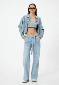 Chaqueta de denim de color azul claro, cortada con bordes deshilachados, combinada con un top crop a juego y pantalones de talle alto sueltos con un detalle de cinturón.