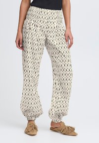 Pantalons amples en tissu crème avec un motif en flèches verticales noires. Dotés d'une taille élastique et d'ourlets à revers.