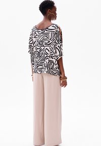 Zwart-wit gemusterde top met een losse pasvorm, gecombineerd met beige wijde broekspijpen. Heeft oversized mouwen en een ronde halslijn.