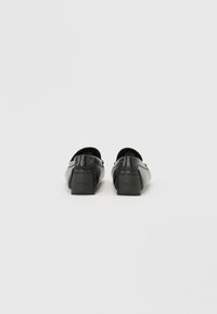 Juodi odiniai slip-on tipo batai su žemu kvadratiniu kulnu. Lygi tekstūra, minimalus siuvinėjimas ir logotipas ant kulno.