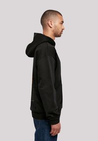 Black hoodie with a kangaroo pocket, ribbed cuffs, and hem. Features a colorful graphic print on the back. Material appears soft and textured.