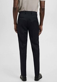 Pantalones negros ajustados con un corte recto, textura suave y dos bolsillos traseros. Combinados con una blusa de color claro y zapatos negros.
