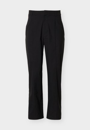 Fekete, karcsúsított nadrág elülső hajtásokkal és derékpánttal, világos háttér előtt.