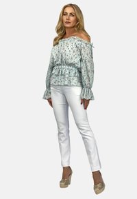 Jasnoniebieska bluzka bez ramiączek w kwiaty z falbaniastym dołem, zestawiona z białymi, dopasowanymi spodniami i brązowymi czółenkami na koturnie. Gładka tekstura materiału.