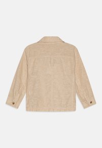 Giacca in lino beige con maniche lunghe, yoke posteriore e polsini a due bottoni. Presenta una texture sottile e un design dalla vestibilità comoda.
