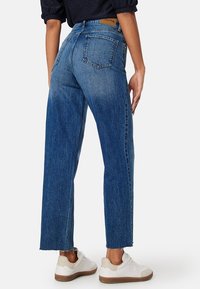 Jeans in denim blu a gamba dritta con vita alta, caratterizzati da un lavaggio sbiadito, design a cinque tasche e orlo sfilacciato, abbinati a sneakers bianche.