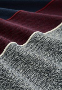 Gewebter Stoff mit einem strukturierten Muster in Marineblau, Burgunderrot und Creme, mit einem glatten, finished Rand und einem leichten Fall.