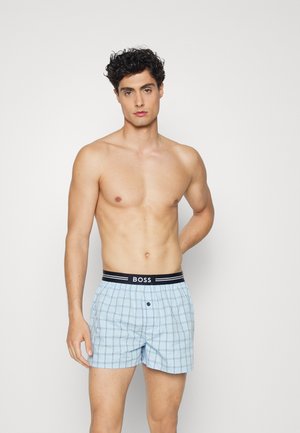 Light blue checked boxers with a black waistband labeled "BOSS." Features a button closure and a loose fit. Smooth fabric texture.