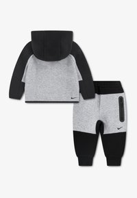 Το σετ δύο τεμαχίων της Nike περιλαμβάνει γκρι και μαύρο μπουφάν με κουκούλα και μαύρη ζώνη με φερμουάρ, καθώς και ταιριαστό παντελόνι φόρμας με τσέπη με φερμουάρ.