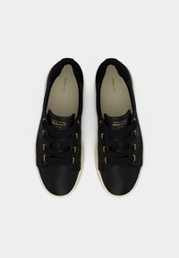 Ζευγάρι μαύρα χαμηλά αθλητικά παπούτσια με μαύρα κορδόνια, μπεζ εσωτερικά πέλματα και λευκές σόλες, σε θέα από πάνω σε ανοιχτό γκρίζο φόντο.