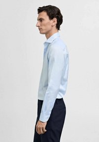 Lichtblauw overhemd met lange mouwen, button-down kraag en een slim fit. Glad textuur aangevuld met donkere broek.