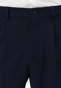 Pantaloni bleumarin dintr-un material texturat, cu închidere cu nasture, buzunare laterale și un design neted al taliei.