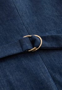 Jeansstoff mit einem gefalteten Riemen, durch eine goldene Doppelring-Schnalle gezogen, der Textur- und Nahtdetails hervorhebt.