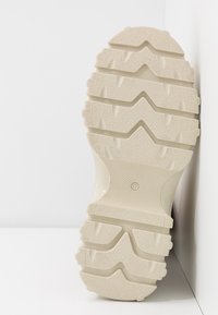 Semelle d'une chaussure beige avec des crampons profonds et texturés et la taille "37" visible au centre sur un fond blanc.