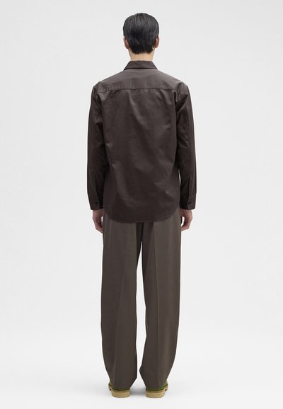 Brun langærmet skjorte med lige snit, som har rygstykke og manchetter. Kombineret med løse brune bukser og sko med grøn sål.