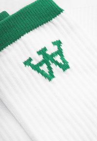 Balti kojinės su žaliu įrubu ir žaliu siuvinėtu logotipu. Audinys turi faktūrinį raštą, su vertikaliomis juostelėmis.