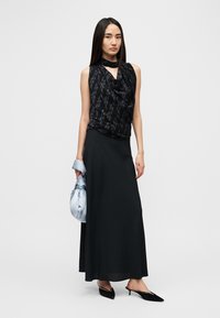 Haut noir sans manches avec un design drapé, associé à une longue jupe noire. Tenant un sac bleu clair à finition satinée et portant des escarpins noirs à bouts pointus.