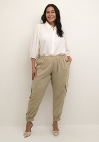 Pantaloni cargo grigi chiari, a vestibilità comoda, con polsini elastici e tasche laterali, abbinati a una camicia bianca con bottoni e maniche a palloncino.