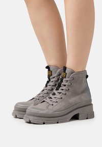 Botas altas grises de ante con suela texturizada, diseño de cordones, herrajes negros y un acento gris en contraste en el talón.