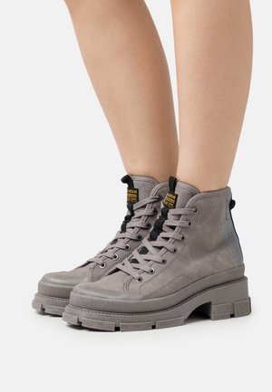 Botas altas grises de ante con suela texturizada, diseño de cordones, herrajes negros y un acento gris en contraste en el talón.