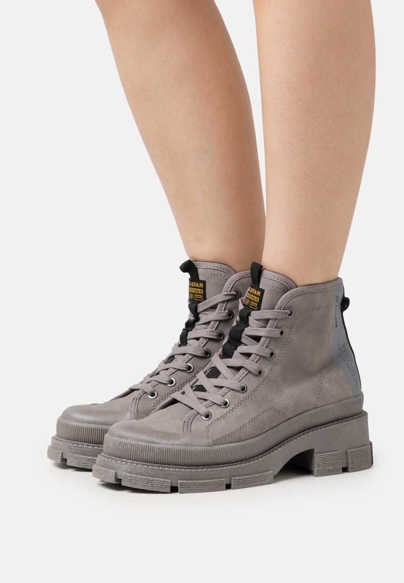 Botas altas grises de ante con suela texturizada, diseño de cordones, herrajes negros y un acento gris en contraste en el talón.