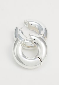 Orecchini a cerchio in argento con finitura lucida, caratterizzati da un design intrecciato con una forma arrotondata e un sottile dettaglio di cucitura.
