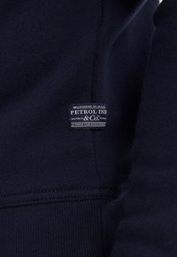 Felpa blu navy realizzata in tessuto testurizzato, con un'etichetta cucita che riporta la scritta "PETROL IND & CO." con testo bianco e blu in un design rettangolare.