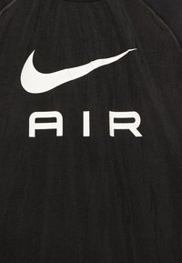 Svart Nike-topp med en stor vit swoosh-logotyp och ordet "AIR" i fet, vita versaler. Lättviktig, strukturerad tyg.