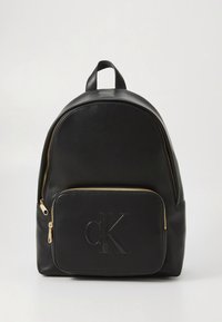 Musta nahkainen reppu pyöreällä muotoilulla, kultasävyisillä vetoketjutikuilla ja etutaskulla, jossa on kohokuvioitu "CK"-logo.