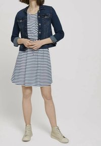 Džínová bunda s dvěma předními kapsami přes námořnické modré a bílé pruhované šaty. Šaty mají stahovací pás a jsou spárovány s béžovými vysokými teniskami.