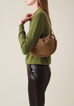 Borsa a tracolla marrone con una texture decorata e un design arricciato, indossata sopra un maglione verde e abbinata a pantaloni di pelle nera.