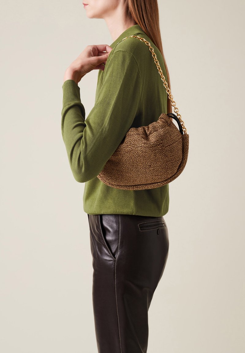 Bolso texturizado marrón con un diseño recogido y una cadena dorada, llevado sobre un suéter verde y combinado con pantalones de piel negros.
