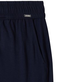 Pantalon à taille élastique bleu marine avec poche latérale et petite étiquette métallique de marque cousue sur la ceinture.