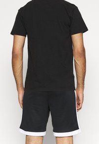 Zwarte katoenen t-shirt met korte mouwen, gecombineerd met zwarte sportshorts met witte strepen langs de zijkanten en een witte rand.