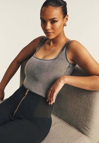 Top sin mangas gris con ribete en contraste, combinado con pantalones negros de tiro alto que presentan un cierre frontal y detalle de malla en la cintura.