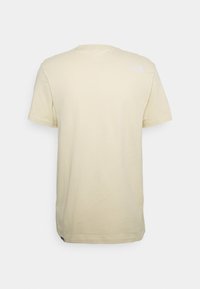 Krátký rukáv tričko z jemné béžové bavlny, s malým bílým logem na horní části zad. Standardní střih, kulatý výstřih, hladká textura.