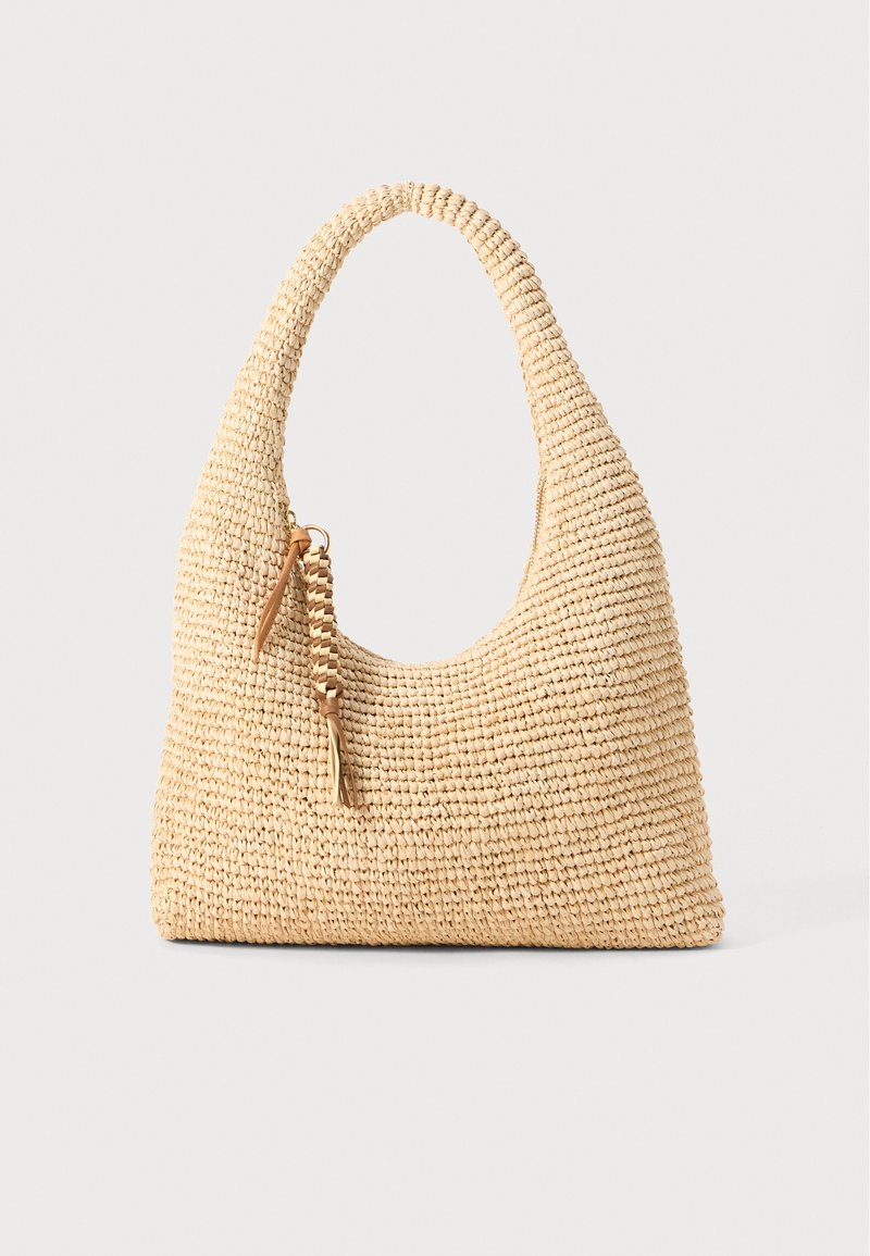 Woven beige handbag with a curved handle, textured surface, and a brown tassel detail. Features a slouchy, hobo shape.