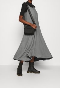 Grå, ärmlös klänning i knälängd av mjukt material med veck; kombinerad med svarta snörkängor och en liten svart crossbody-väska.