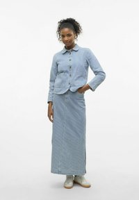 Prugasta modra kavbojka z gumbi in dvema sprednjima žepoma, v kombinaciji z dolgo ujemajočo se krilo. Obe oblačili imata sproščen kroj.