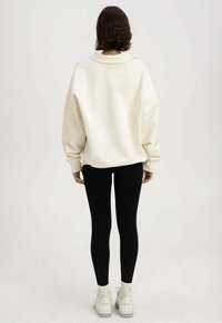 Overmaatse crèmekleurige sweatshirt met een hoge kraag, gecombineerd met zwarte leggings en witte chunky sneakers. Gladde stof, casual ontwerp.