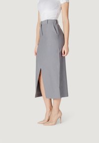 Falda midi gris con una abertura frontal, diseño ajustado y bolsillos laterales, combinada con zapatos de tacón nude y una blusa blanca de canalé.