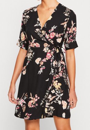 Schwarzes Wickelkleid mit pinken, gelben und weißen Blumenmustern, kurzen Ärmeln und einem gebundenen Taillendetail an einer stehenden Person.