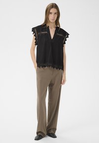 Juodas viršus su V formos iškirpte ir trumpomis banguotomis rankovėmis, puoštas lazeriu pjaustytomis detalėmis. Derinamas su smėlio spalvos dryžuotomis kelnėmis ir juodais batais.