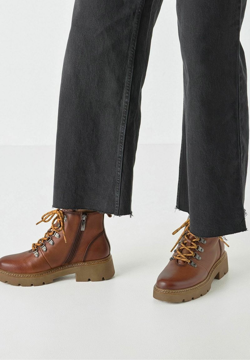 Bottes cheville en cuir marron avec une finition texturée, dotées d'une fermeture éclair, d'un bout rond et d'une semelle épaisse. Lacets marron et orange avec œillets en métal.