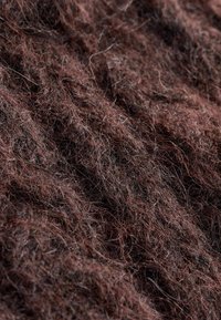 Hnědá textilie s jemnou, nepravidelnou strukturou. Vlákna jsou hrubá a různě dlouhá, což vytváří měkký a teplý vzhled.