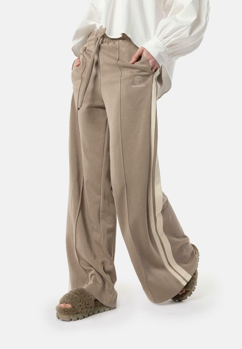 Beige wide-leg sweatpants with side stripes, elastic waistband, and pockets. Soft material with a relaxed fit. Paired with fluffy slides.