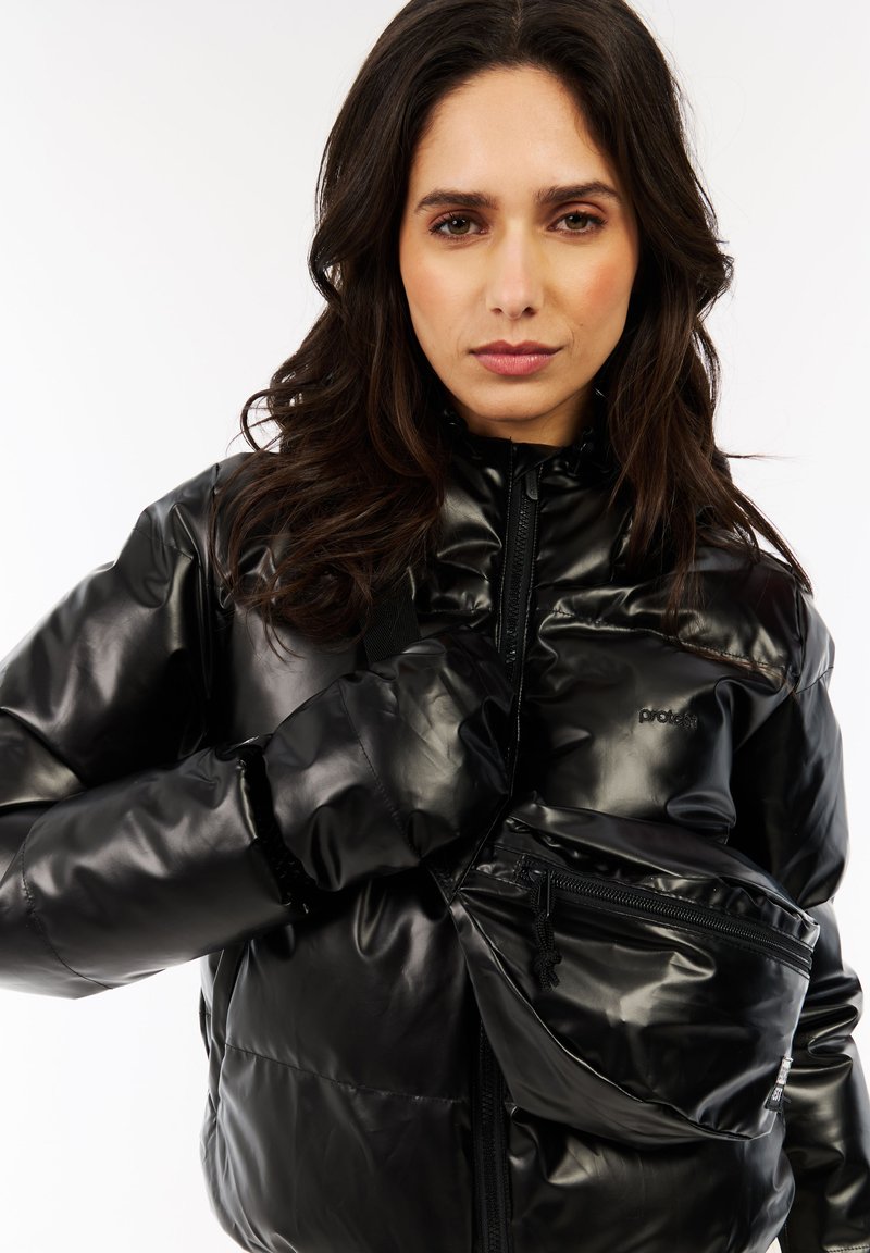 Sort polstret jakke med skinnende, glat tekstur, der har en høj krave, lynlås lukning og en lynlåslomme foran. Brandlogoet er synligt.